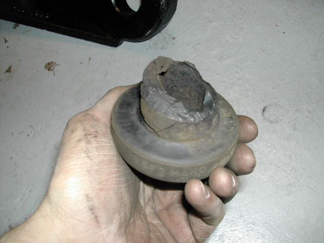 Hand holding a worn rubber bushing marked LEFT HAND with damaged center sleeve