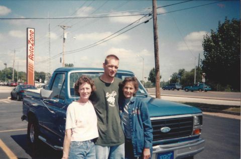 1982 Ford Bronco - A teal Ford pickup truck is shown from the front-three-quarter view, with three people posing in front of it.
