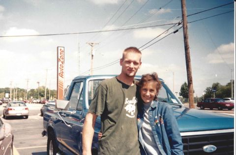1982 Ford Bronco - A man and woman pose in front of a blue pickup truck, with an AutoZone store visible behind them.