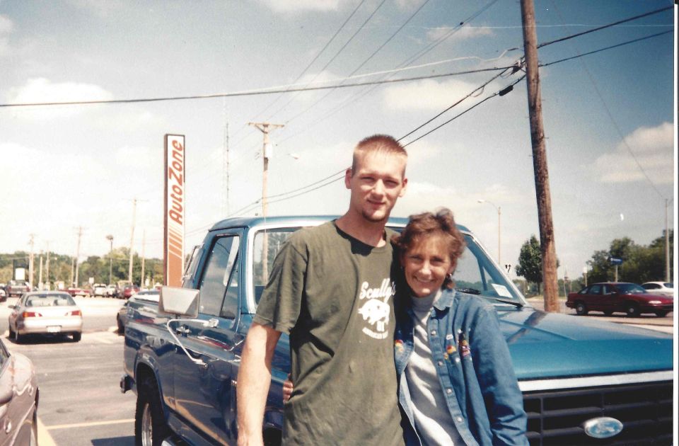 Blue pickup truck with a man and woman in front, AutoZone sign in background