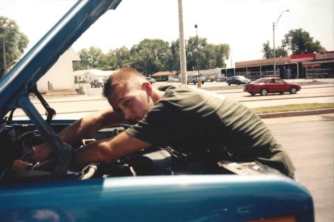 1982 Ford Bronco - Man works on the engine of a blue vehicle with the hood open.