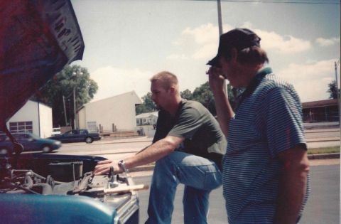 1982 Ford Bronco - Two men are gathered around the open hood of a car, appearing to work on the engine.