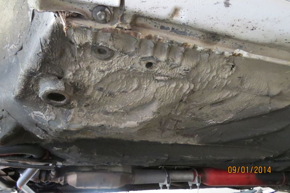 Undercarriage of a car showing rust and damage, with exhaust pipe visible