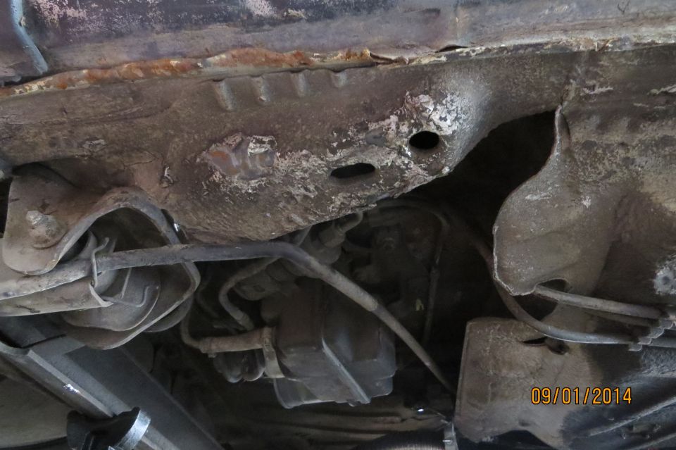 Undercarriage of a rusty car with visible suspension components and exhaust system