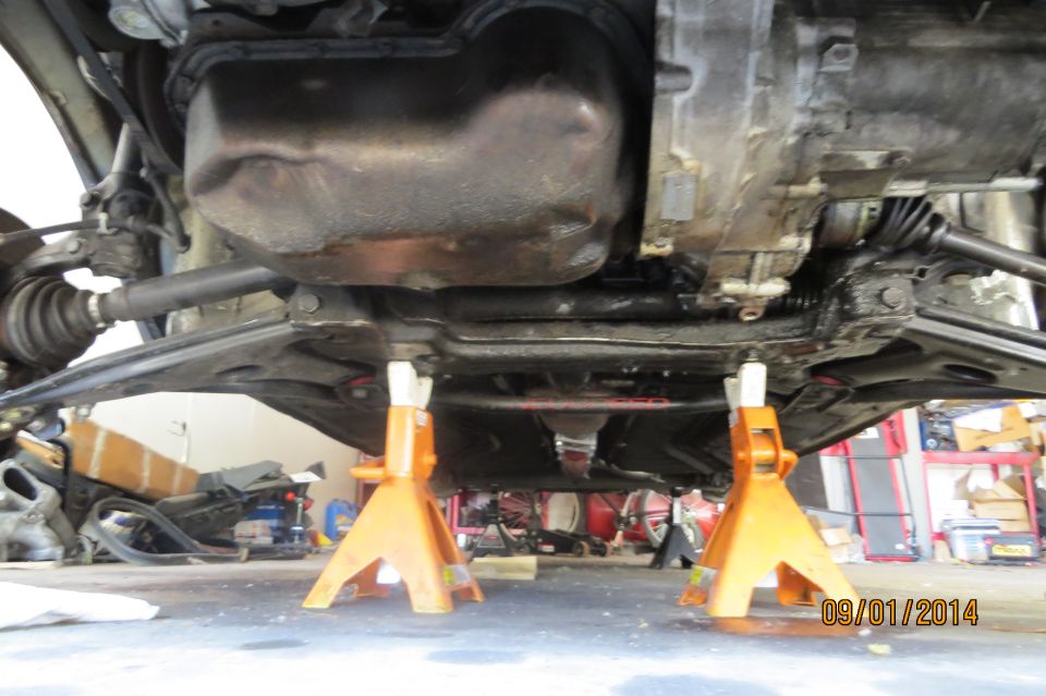 Underbody view of a car on jack stands, showing suspension and drivetrain components