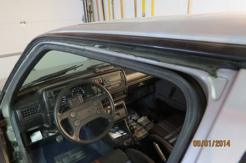 1985 Volkswagen GTI interior showing dashboard, steering wheel with GTI logo, and plaid seats