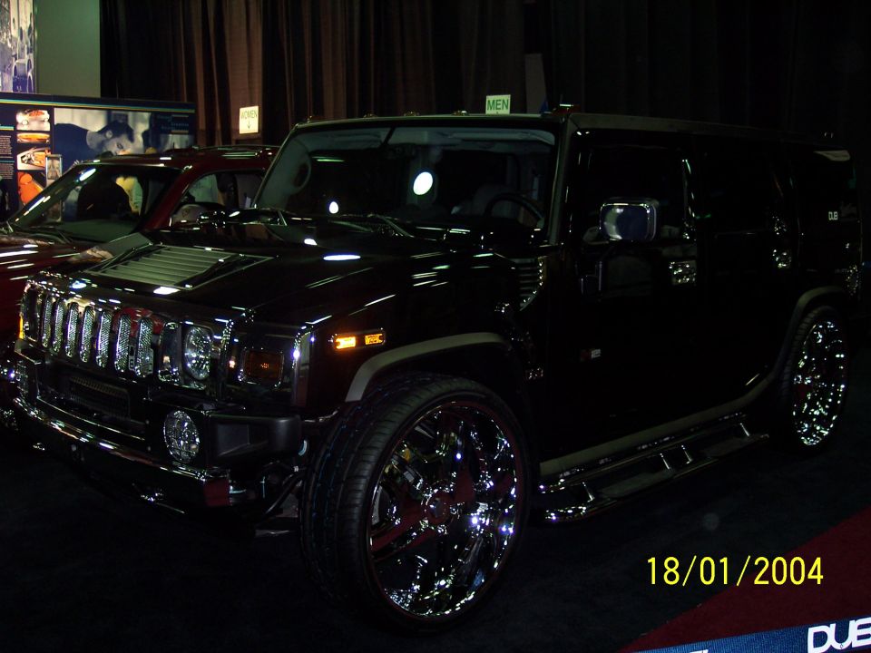Black Hummer H2 with chrome rims and running boards, parked next to a red car