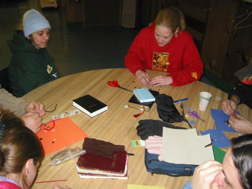 People gathered around a round table, engaged in craft activities with various supplies like scissors, paper, and books