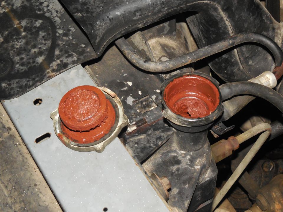 Radiator cap and filler neck caked with thick reddish-brown coolant residue in a dirty engine bay