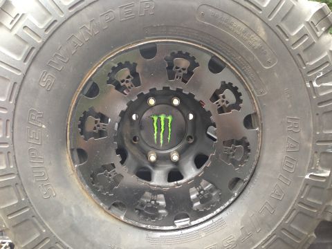 1979 Ford Bronco - This custom wheel features skull and gear cutouts and a Monster Energy logo, mounted on a Super Swamper radial tire.