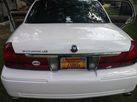 2000 Mercury Grand Marquis - The rear of a white Mercury Grand Marquis, showing the license plate and various stickers on the window and bumper.