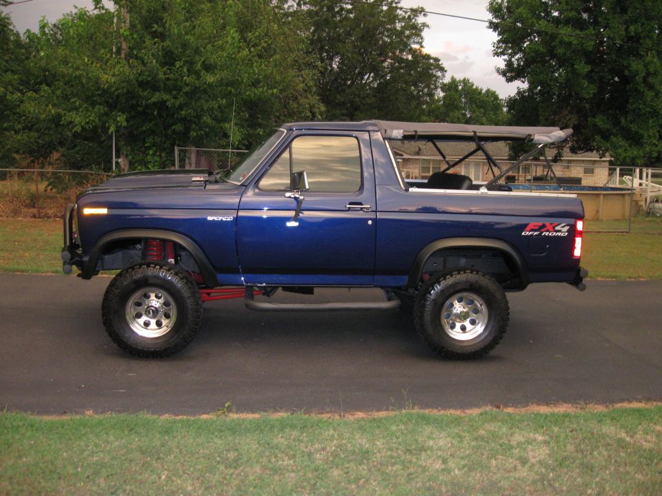 Blue 1980s Ford Bronco with a soft top and lifted suspension, viewed from the side