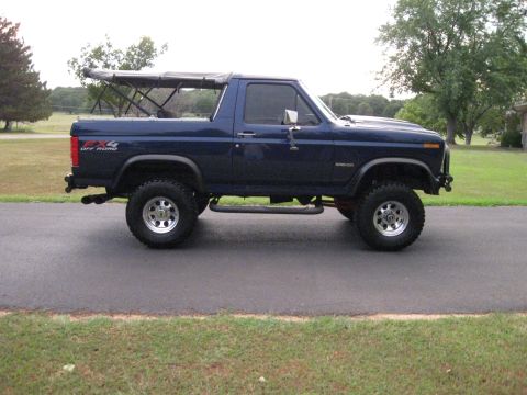 1982 Ford Bronco - This blue Ford Bronco is shown from the side with its top down, parked on a paved surface.