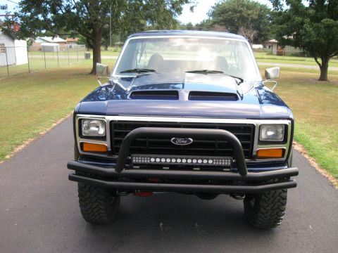 1982 Ford Bronco - This blue Ford Bronco is parked on a driveway with a grassy yard and trees in the background.