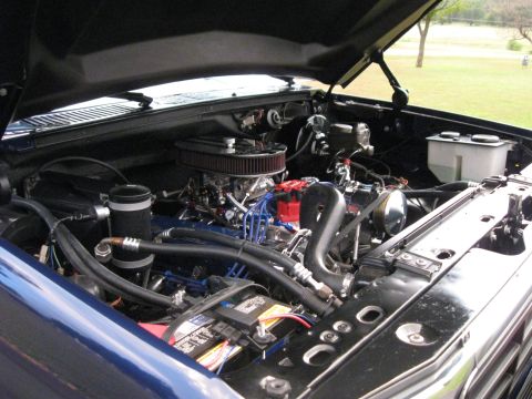 1982 Ford Bronco - The engine bay of a blue Ford Bronco shows aftermarket modifications and a clean setup.