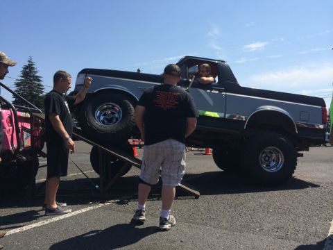 1989 Ford Bronco - A lifted Ford Bronco is positioned on a ramp at an outdoor event, with several people observing.