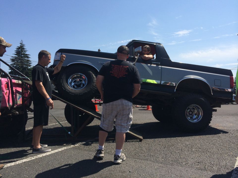 Gray and black Ford Bronco with lifted suspension on a ramp, driver visible, chrome wheels
