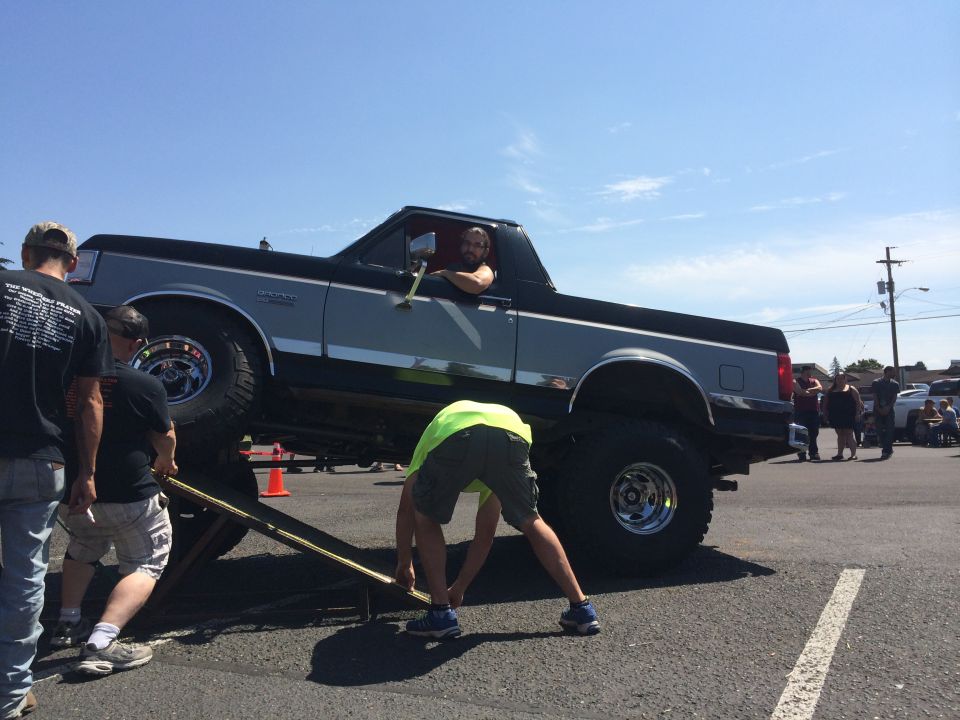 1989 Ford Bronco being lifted by a jack with people around it