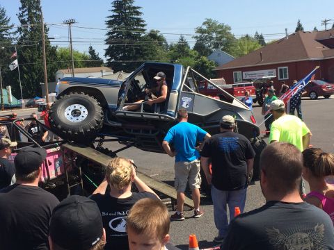 1989 Ford Bronco - A heavily modified truck is displayed on a ramp at an outdoor event with spectators gathered around.