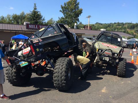 1989 Ford Bronco - Two heavily modified off-road trucks are displayed at an outdoor event.