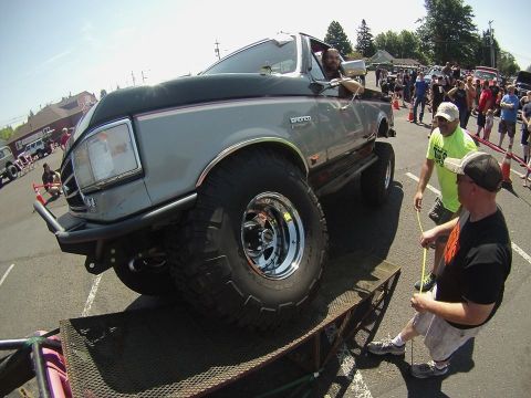 1989 Ford Bronco - A modified Ford Bronco is positioned on a ramp at an outdoor event with spectators watching.