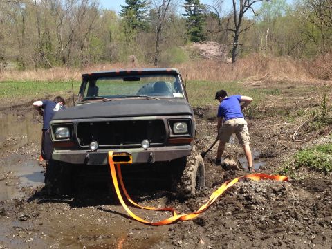 1979 Ford Bronco - A black Ford Bronco is stuck in the mud with two people attempting to dig it out.