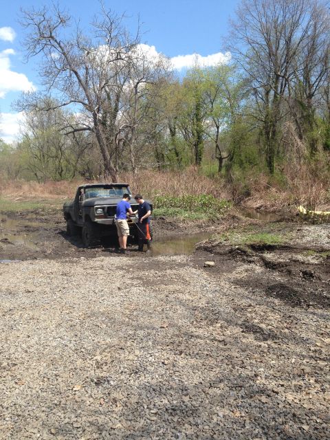 1979 Ford Bronco - Two people attempt to free a dark 1979 Ford Bronco that is stuck in a muddy ditch.