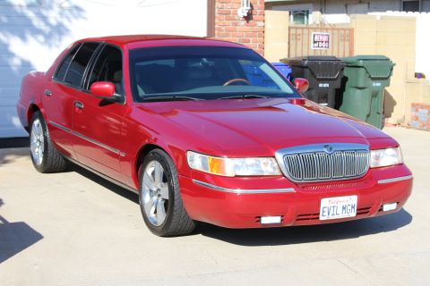 2002 Mercury Grand Marquis - A red 2002 Mercury Grand Marquis is parked in front of a garage with trash cans nearby.