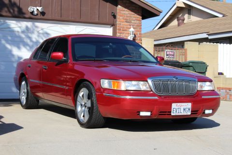 2002 Mercury Grand Marquis - A red 2002 Mercury Grand Marquis is parked in front of a garage, showing its grille and front end.
