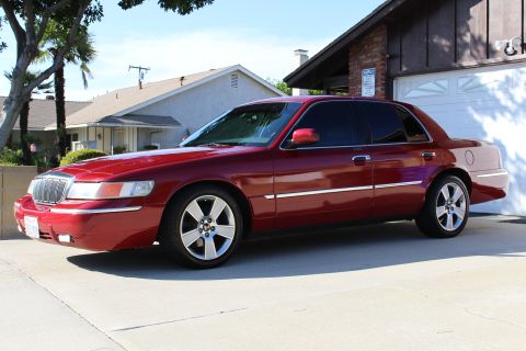 2002 Mercury Grand Marquis - This red 2002 Mercury Grand Marquis sedan is shown from a three-quarter front angle, parked in front of a garage.