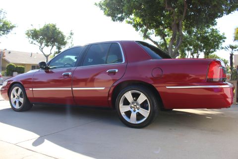 2002 Mercury Grand Marquis - A red 2002 Mercury Grand Marquis sedan is parked on a concrete driveway under a tree.