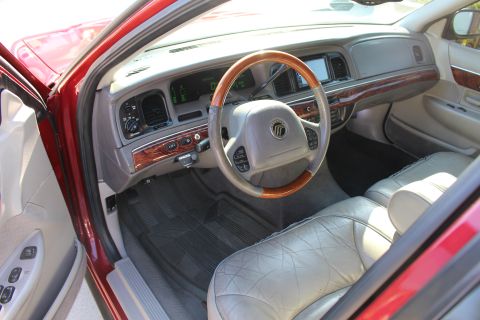 2002 Mercury Grand Marquis - The interior of a red Mercury Grand Marquis features light-colored leather seats and wood trim accents on the dashboard and steering wheel.