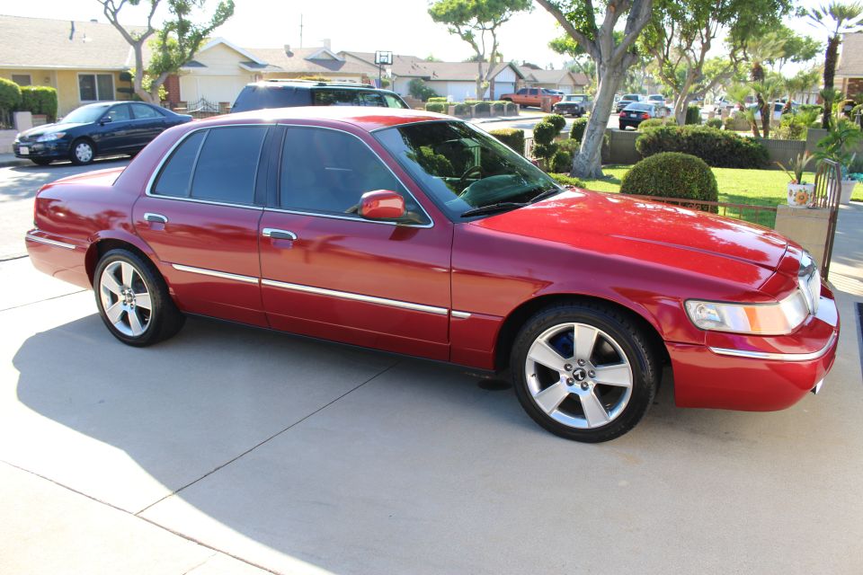 red 2002 Mercury Grand Marquis parked on driveway, other cars and houses in background