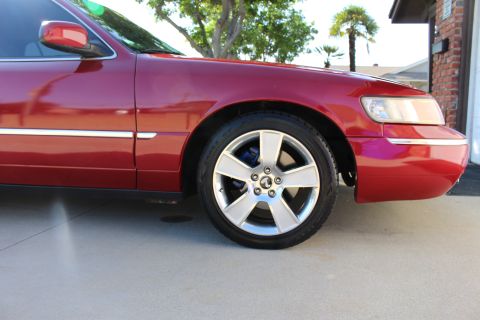 2002 Mercury Grand Marquis - Front passenger side view of a red sedan with aftermarket wheels and chrome trim.