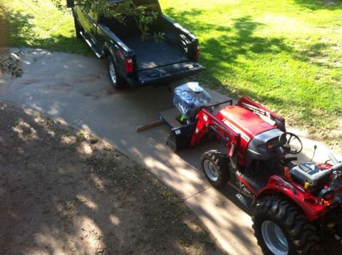 1982 Ford Bronco - A black pickup truck is seen towing a red tractor and an engine on a trailer.