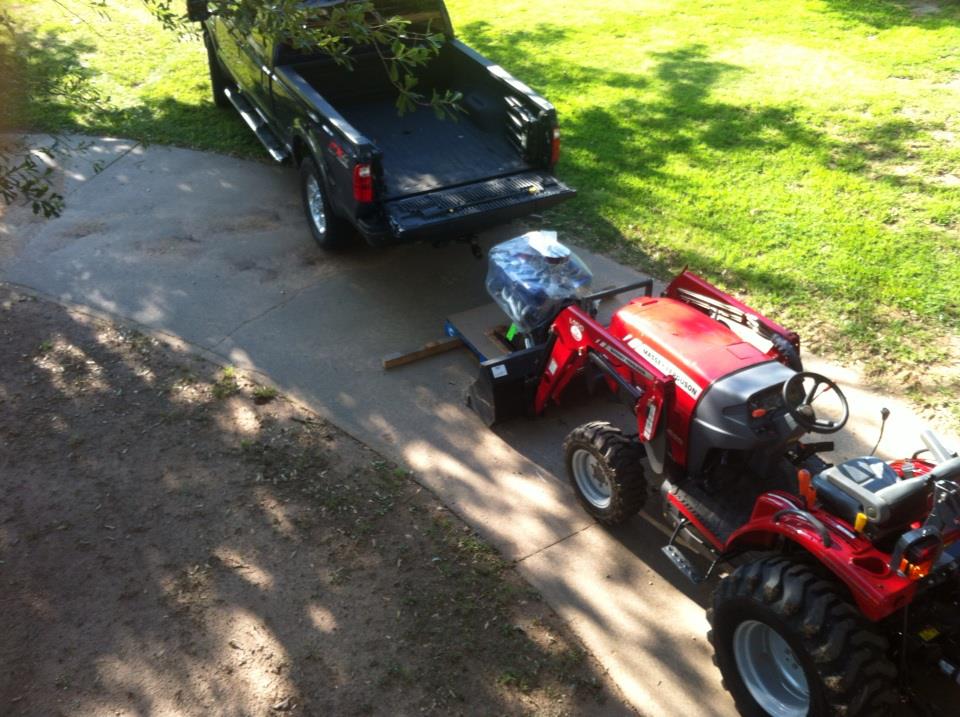 Black pickup truck towing a red tractor and an engine on a trailer
