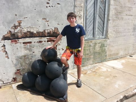 2007 Ford F-250 - A young boy stands next to a pyramid of cannonballs, with a textured wall and wooden shutters behind him.