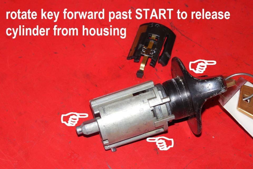 Ignition lock cylinder with key on red mat, annotated with instructions for releasing it from the housing