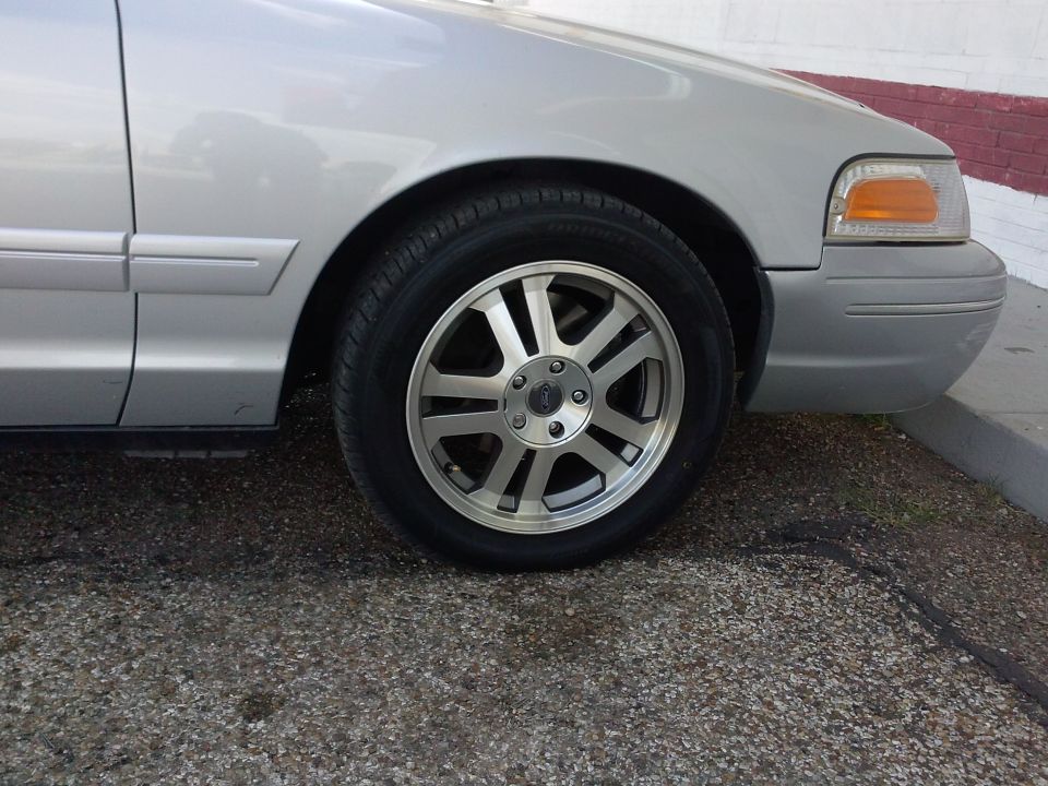 Silver sedan's front passenger side wheel and fender. The car has a chrome trim strip along the lower door