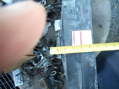 1980 Ford Bronco - A radiator support is measured with a tape measure, revealing a label with red and white text.