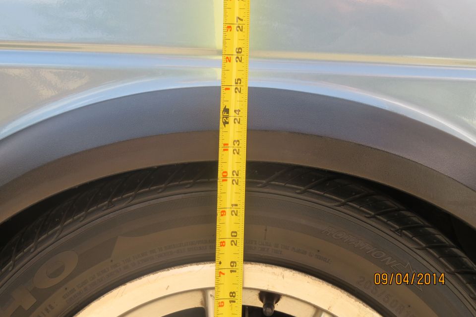 Close-up of a car's wheel well and tire, with a yellow measuring tape indicating height