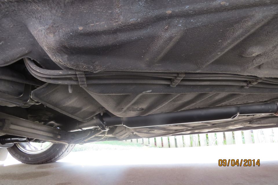 Underside view of a car, showing fuel lines and exhaust pipe. A tire is visible on the left