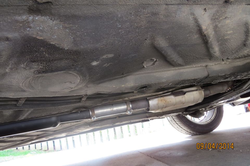 Underside of a car showing exhaust pipes and a catalytic converter, with a tire visible on the right