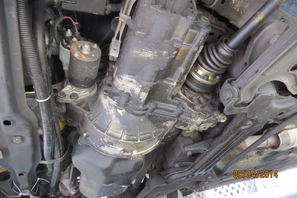 Underside of a vehicle showing a greasy transmission, starter motor, and CV axle