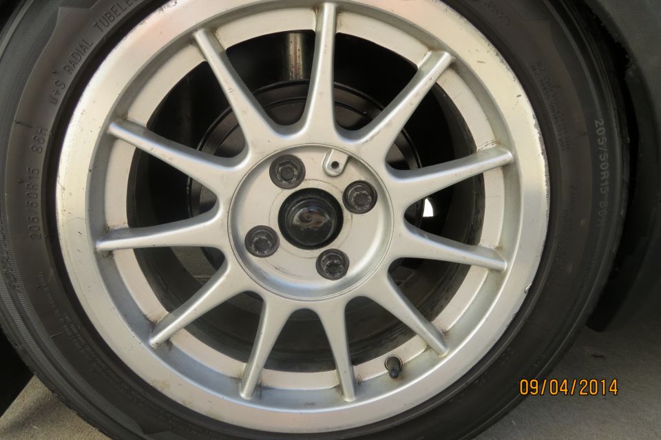 Close-up of a silver 5-spoke alloy wheel with a tire. Tire size 205/50R15 is visible