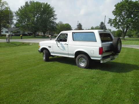 1996 Ford Bronco - A white Ford Bronco is parked on a green lawn with houses and trees in the background.