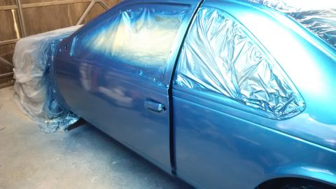 1994 Ford Thunderbird - A blue car is masked and being painted in a garage.