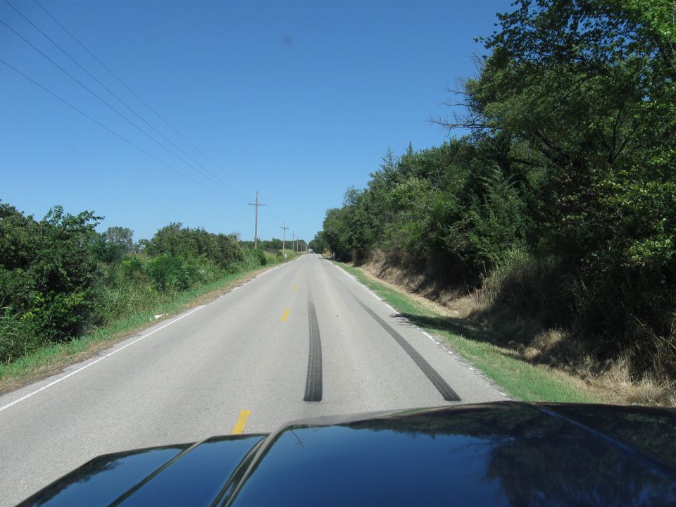 View from a vehicle looking down a rural road with tire tracks and trees lining the sides