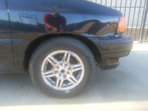 1991 Ford Festiva - Close-up of the front passenger side of a black hatchback, showing the wheel and fender detail.