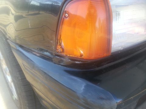 1991 Ford Festiva - Close-up of a black car's front corner, showing the amber turn signal and part of the headlight assembly. The Supermotors.net logo is visib…